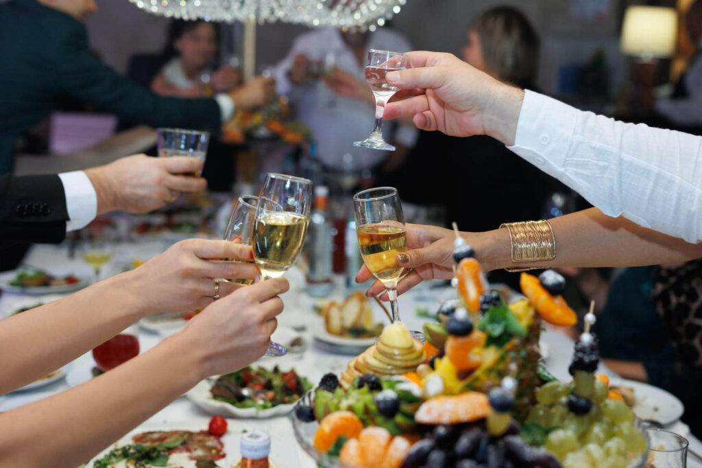 Guests clinking champagne glasses in a toast over a banquet table filled with food and fruit arrangements